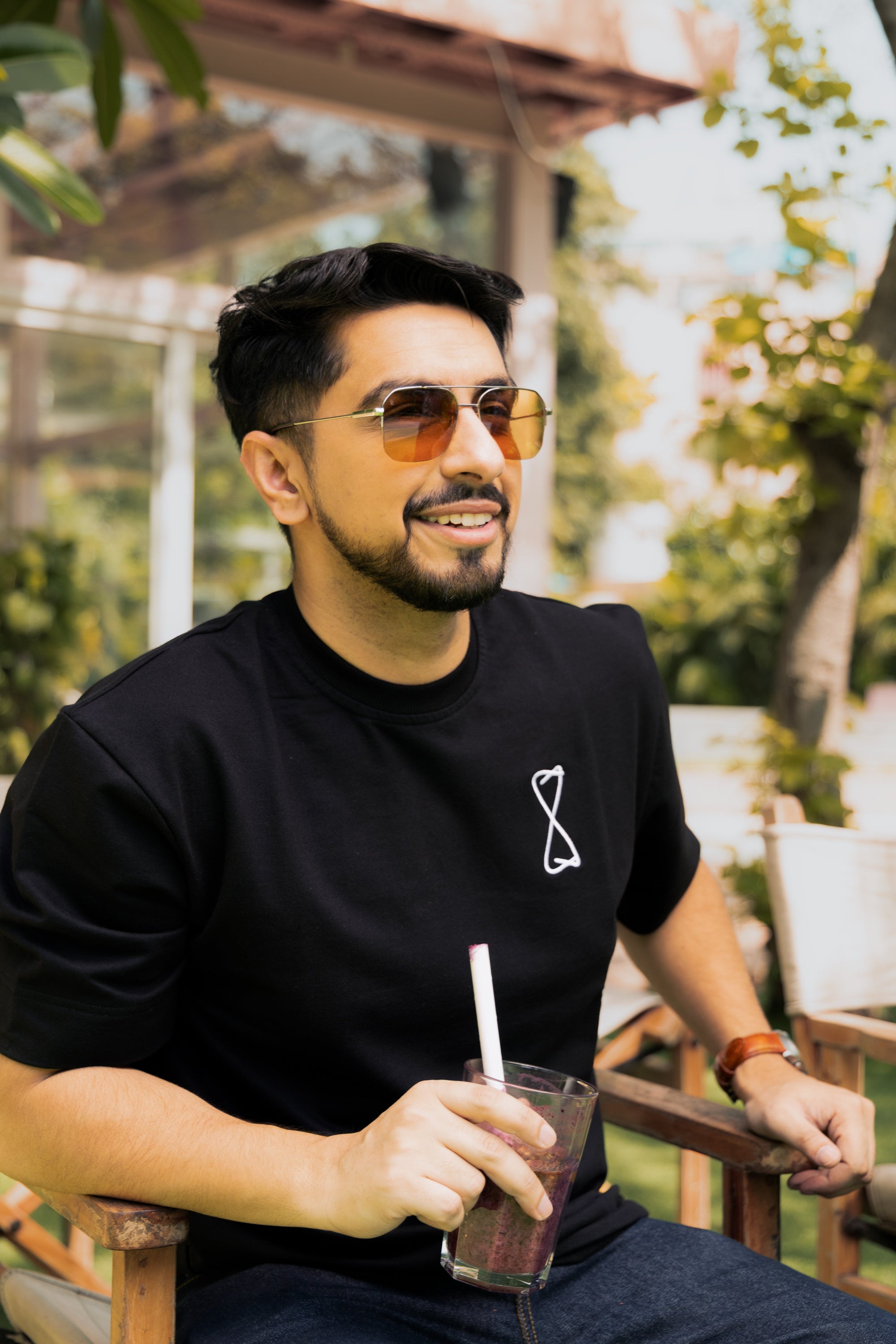 Man wearing sunglasses and a black t-shirt with a straw drink outdoors